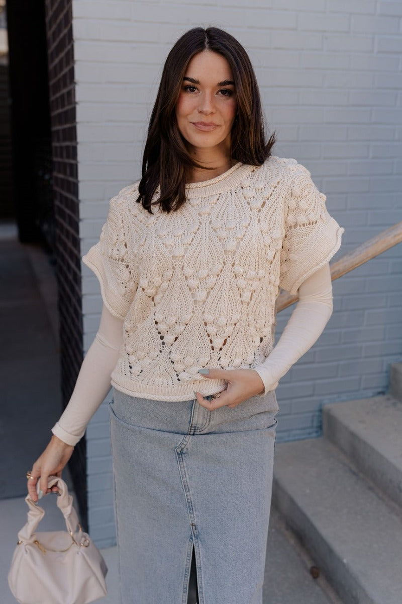 Front view of model wearing the Megan Cream Crochet Short Sleeve Sweater that has cream crochet knit fabric, 3d polka dots, ribbed hem, round neck, and short sleeves. Worn over long sleeve top.