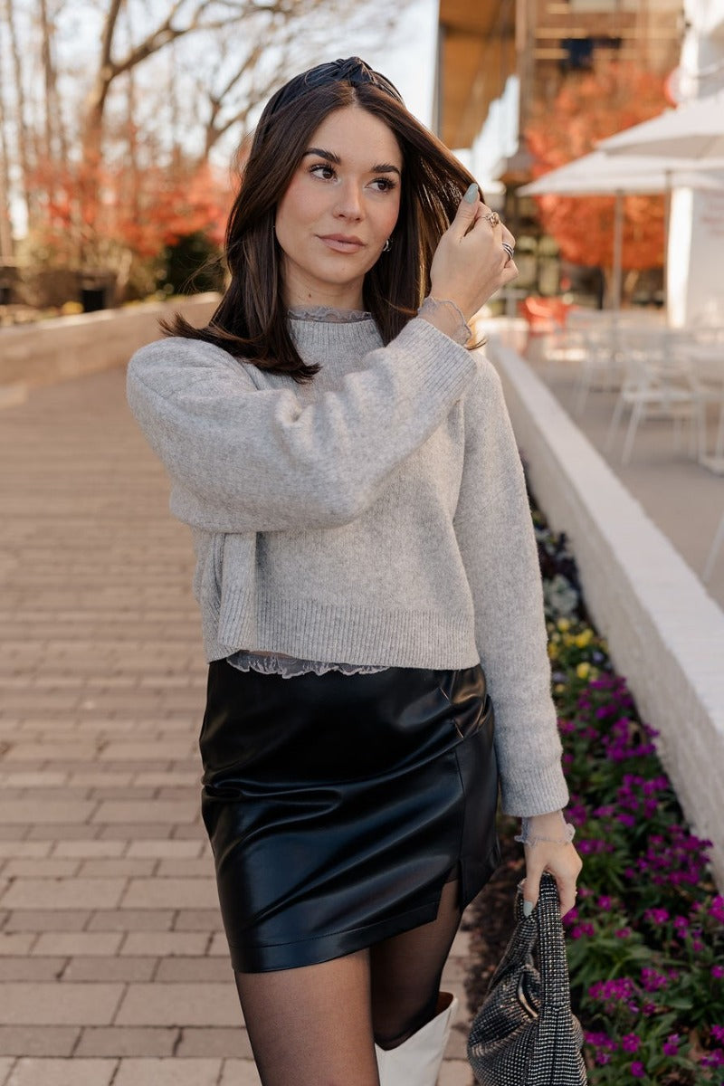 front view of model wearing the Emily Grey Cropped Long Sleeve Sweater that has heather grey knit fabric, ribbed hem, cropped waist, a high neck, dropped shoulders, and long sleeves.