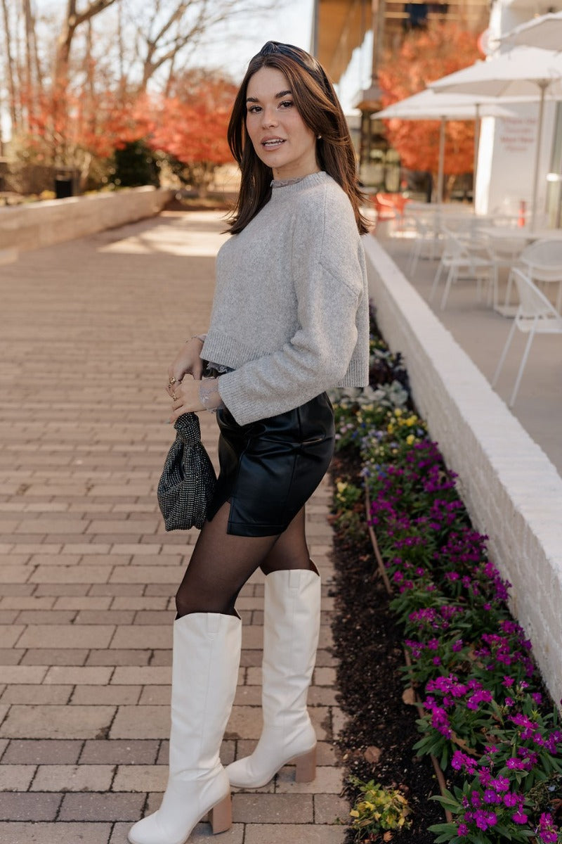 Full body side view of model wearing the Emily Grey Cropped Long Sleeve Sweater that has heather grey knit fabric, ribbed hem, cropped waist, a high neck, dropped shoulders, and long sleeves.