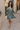 Full body view of model wearing the Maya Olive Satin Ruffle Long Sleeve Dress which features olive grey satin fabric, mini length, ruffle details, a three-tier design, olive grey lining, a plunge neckline, long sleeves with elastic cuffs, and a back key h