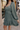 Side view of model wearing the Maya Olive Satin Ruffle Long Sleeve Dress which features olive grey satin fabric, mini length, ruffle details, a three-tier design, olive grey lining, a plunge neckline, long sleeves with elastic cuffs, and a back key hole w