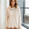 Front view of model wearing the New You Striped Sweater that has a cream and light brown striped pattern, a light brown ribbed high-low hem, a cowl neckline, and long sleeves with light brown ribbed wrists.