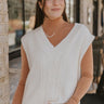 front view of model wearing the Whitney Sweater Vest in Ivory that has cream knit fabric with cable knit details, slits on each side, a v neckline and a sleeveless body. 