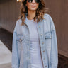 Front view of model wearing the Should've Known Shacket that has light-wash denim fabric, two front chest pockets, a button-up front, a collar, a frayed hem and long sleeves.
