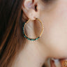 Close view of model wearing the Under The Sea Earrings that have light green and teal beads with clear stones, set in a gold hoop.