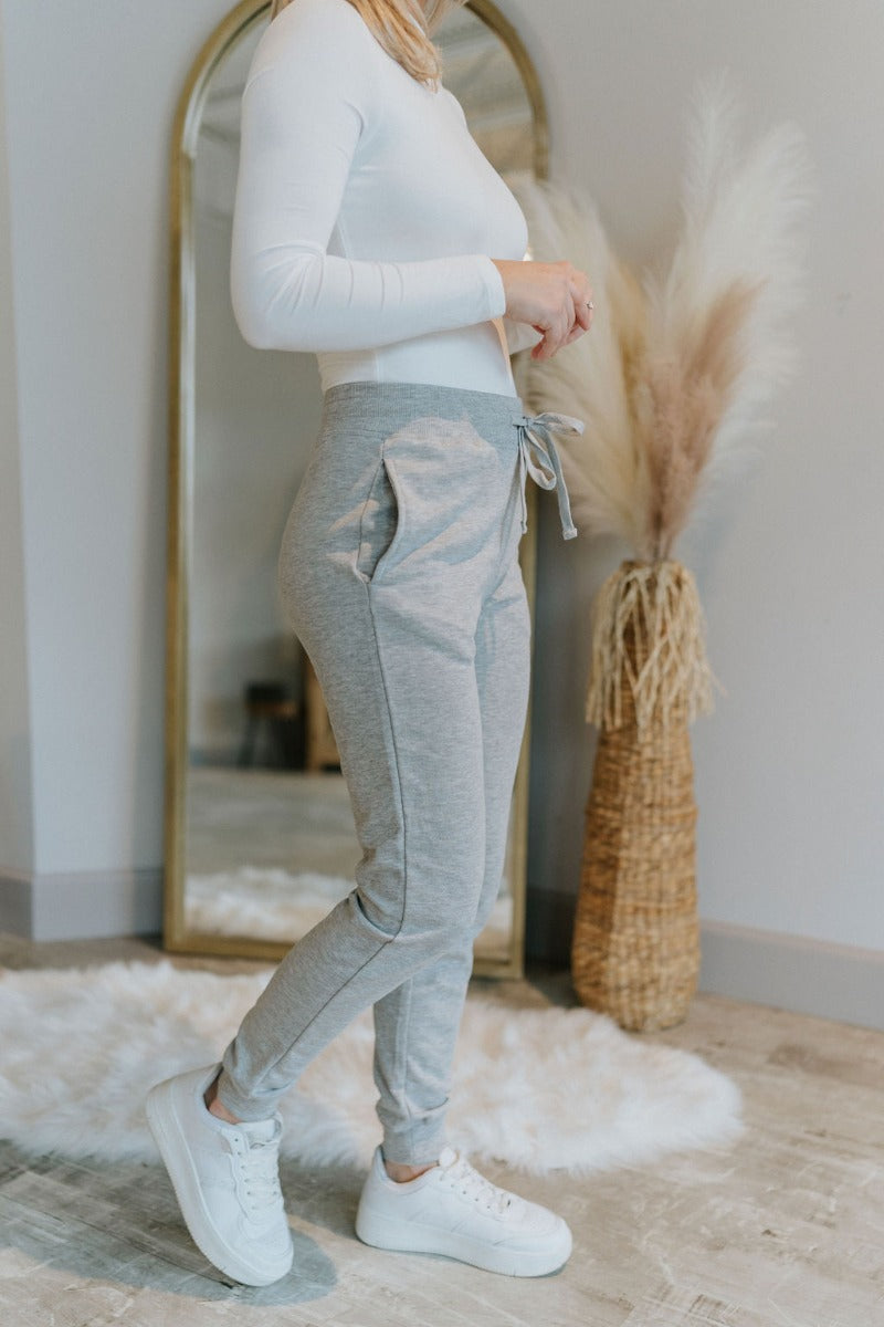 Side view of model wearing the Everyday Dreams Pants which features heather grey fabric, two side pockets, an elastic drawstring waist, and jogger legs with elastic ankles.