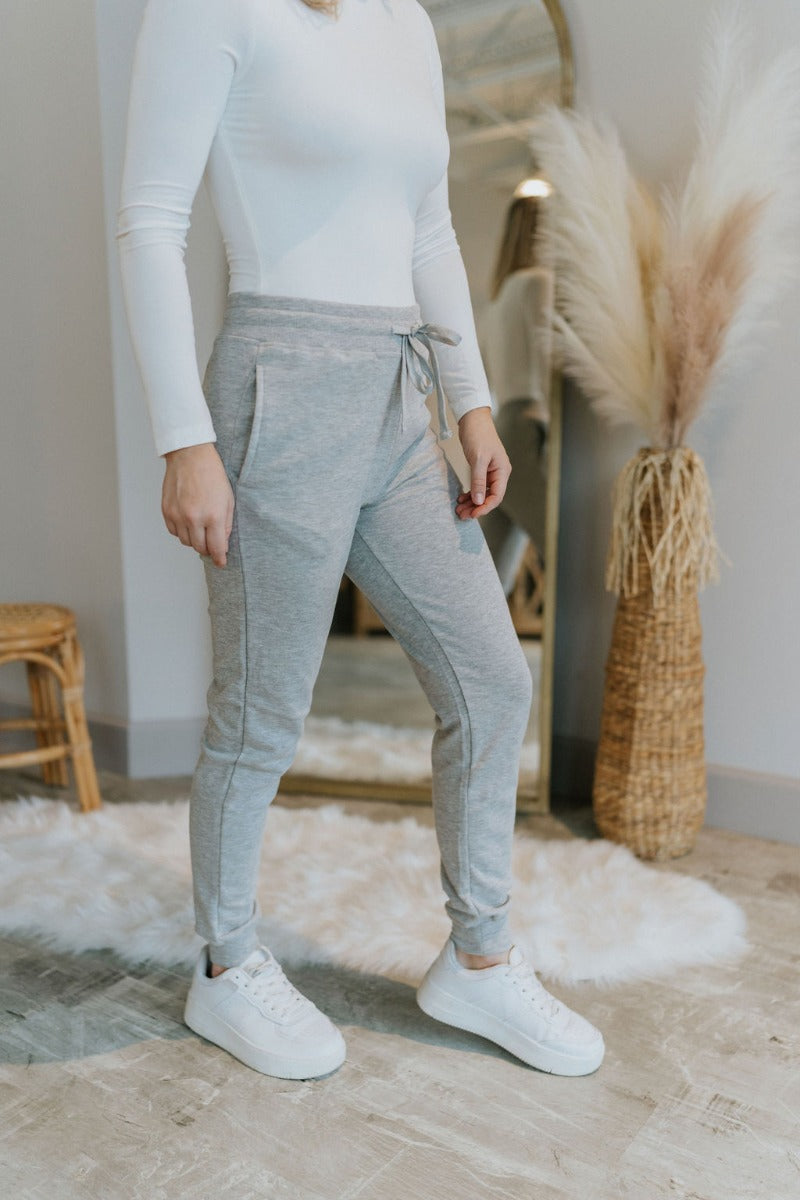 Side view of model wearing the Everyday Dreams Pants which features heather grey fabric, two side pockets, an elastic drawstring waist, and jogger legs with elastic ankles.