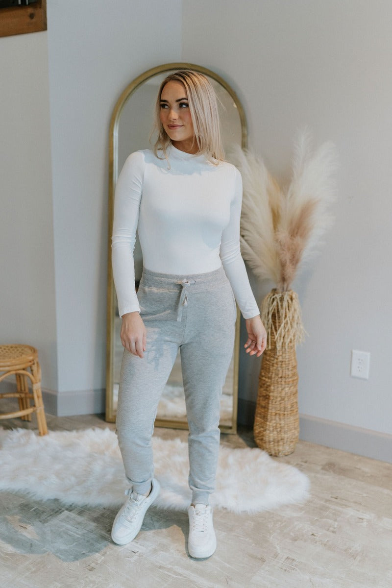 Full body view of model wearing the Everyday Dreams Pants which features heather grey fabric, two side pockets, an elastic drawstring waist, and jogger legs with elastic ankles.
