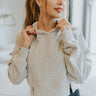 Close front view of model wearing the Next Level Hoodie that has heather grey knit fabric, a cropped waist with slits on each side, ribbed trim, a round neckline with a hood, dropped shoulders, and long sleeves
