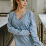 Front view of model wearing the Let's Stay In Top that has light blue fabric, a  notched round neckline, long sleeves, and ribbed trim