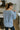 Back view of model wearing the Let's Stay In Top that has light blue fabric, a  notched round neckline, long sleeves, and ribbed trim