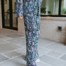 Side view of model wearing the Crazy In Love Pants that have black plisse fabric with a multi-color floral pattern, an elastic waist band, and wide legs with lettuce trim