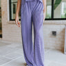 Front view of model wearing the Wanderlust Pants that feature purple plisse fabric, an elastic waistband, and wide legs with lettuce trim