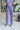Front view of model wearing the Wanderlust Pants that feature purple plisse fabric, an elastic waistband, and wide legs with lettuce trim