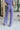 Back view of model wearing the Wanderlust Pants that feature purple plisse fabric, an elastic waistband, and wide legs with lettuce trim