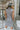Back view of model wearing the Call Me Later Sweater Dress that has grey knit fabric, a mini length hem, a loose turtleneck, and a sleeveless body.