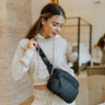 Front view of model wearing the On The Go Sling Bag in Black which features black coloring fabric, three openings with black zippers and black adjustable strap for a cross-body look.