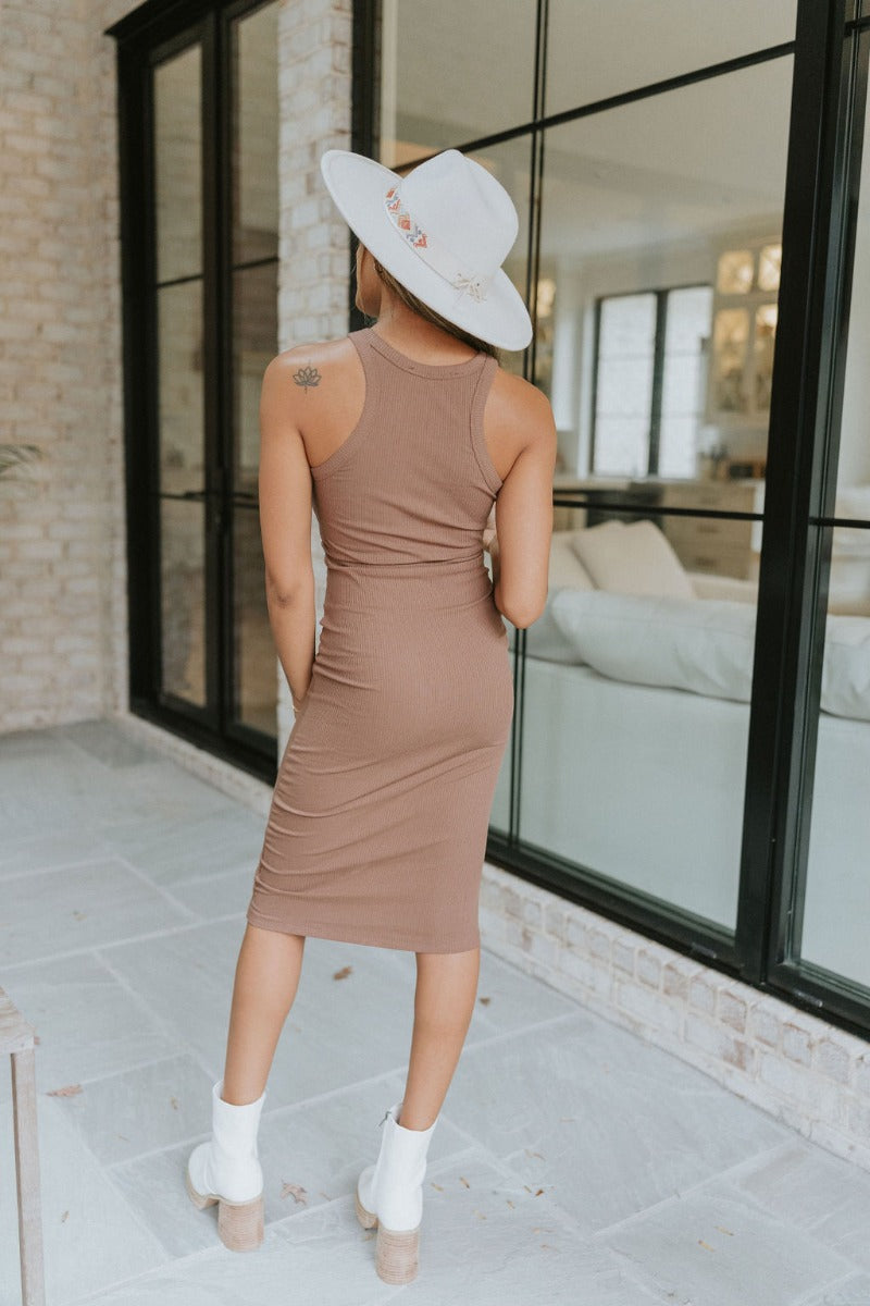 Back view of model wearing the Walk Of Fame Dress in Brown that has brown ribbed fabric, a midi-length hem, a high neckline, and a sleeveless body.