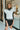 Front view of model wearing the Walk The Line Sweater Vest in White that has white knit fabric, ribbed trim with black stripes, a v-neckline and a sleeveless body