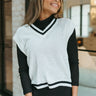Front view of model wearing the Walk The Line Sweater Vest in White that has white knit fabric, ribbed trim with black stripes, a v-neckline and a sleeveless body