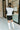 Back view of model wearing the Walk The Line Sweater Vest in White that has white knit fabric, ribbed trim with black stripes, a v-neckline and a sleeveless body