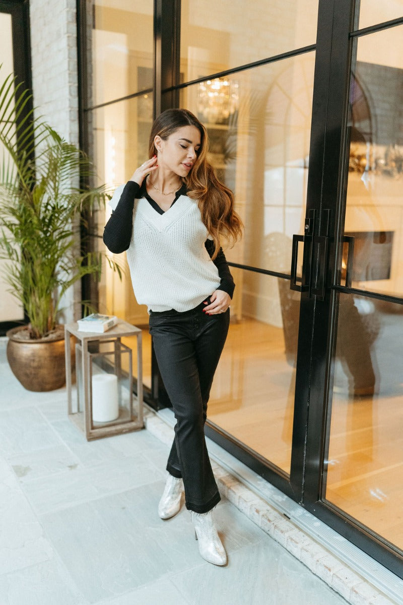 Full body front view of model wearing the KanCan: Trend Report Jeans that have black sheen denim fabric, a 5-button closure, two pockets, back pockets, belt loops, high-rise waist, and cropped flare legs with a raw hem