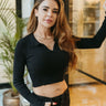 Front view of model wearing the Downtown Days Top in Black that has black ribbed fabric, a cropped waist, a v neckline with a collar, and long sleeves