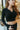 Front view of model wearing the Downtown Days Top in Black that has black ribbed fabric, a cropped waist, a v neckline with a collar, and long sleeves