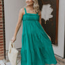 Full body view of model wearing the No More Wishing Dress which features kelly green fabric with a lining, a tiered midi-length skirt, a ruched neckline, adjustable thick straps, and a smocked back.