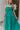 Close up view of model wearing the No More Wishing Dress which features kelly green fabric with a lining, a tiered midi-length skirt, a ruched neckline, adjustable thick straps, and a smocked back.