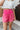 Close front view of model wearing the Let's Get Away Shorts that have hot pink acid wash fabric, a frayed hem, two side pockets, two back pockets, and an elastic high-rise waistband