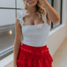 Front view of model wearing the It's Complicated Satin Skort in Red that has red satin fabric, a tiered body with ruffle details, an elastic drawstring waist, and shorts lining.