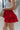 Side view of model wearing the It's Complicated Satin Skort in Red that has red satin fabric, a tiered body with ruffle details, an elastic drawstring waist, and shorts lining.