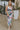 Front view of model wearing the In Bloom Midi Dress that has white fabric with a purple, blue, green and pink watercolor floral design, ruching, a v-neck, thick straps, a a side slit, and a lining