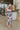 Front view of model wearing the In Bloom Midi Dress that has white fabric with a purple, blue, green and pink watercolor floral design, ruching, a v-neck, thick straps, a a side slit, and a lining