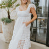 Front view of model wearing the Picture Perfect Midi Dress in White that has sheer white fabric with a checkered pattern, a white lining, a tiered midi-length body, side pockets, and tiered cap sleeves.
