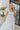 Front view of model wearing the Picture Perfect Midi Dress in White that has sheer white fabric with a checkered pattern, a white lining, a tiered midi-length body, side pockets, and tiered cap sleeves.