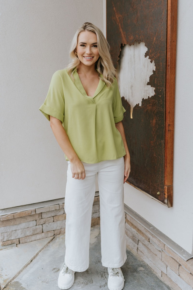Full body view of model wearing the Where Have You Been Pants which features white denim fabric, two front pockets, two back pockets, belt loops, a front button and zipper closure, and cropped flare legs.
