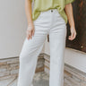 Close up view of model wearing the Where Have You Been Pants which features white denim fabric, two front pockets, two back pockets, belt loops, a front button and zipper closure, and cropped flare legs.