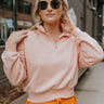 Front view of model wearing the Coastal Breeze Pullover that has peach colored fabric, a cropped waist, a monochromatic quarter zip-up, a high neckline, and long sleeves with cuffs