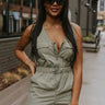Front view of model wearing the Fair Game Romper that has army green fabric, front chest pockets, a front zipper , an elastic waist with drawstrings, side pockets, back pockets, a v neck, and thick straps