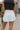 Back view of model wearing the Step It Up Skort in White that has white fabric, shorts lining, a v overlap waistline, slits on each side, and a mini-length hem