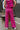Back view of model wearing the On The West Coast Pants that feature fuchsia fabric with a textured line design, two front pockets, an elastic waistband, and flared legs.