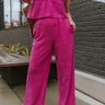 Front view of model wearing the On The West Coast Pants that feature fuchsia fabric with a textured line design, two front pockets, an elastic waistband, and flared legs.