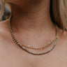 Close up image of model wearing the Should've Known Necklace that has a double gold chain with iridescent grey and gold beads.