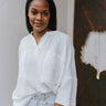 Front view of model wearing the Bring Back Summer Top in White which features off white gauze fabric, an oversized fit, two front chest pockets, a v cutout with a round neckline, dropped shoulders, and short sleeves.