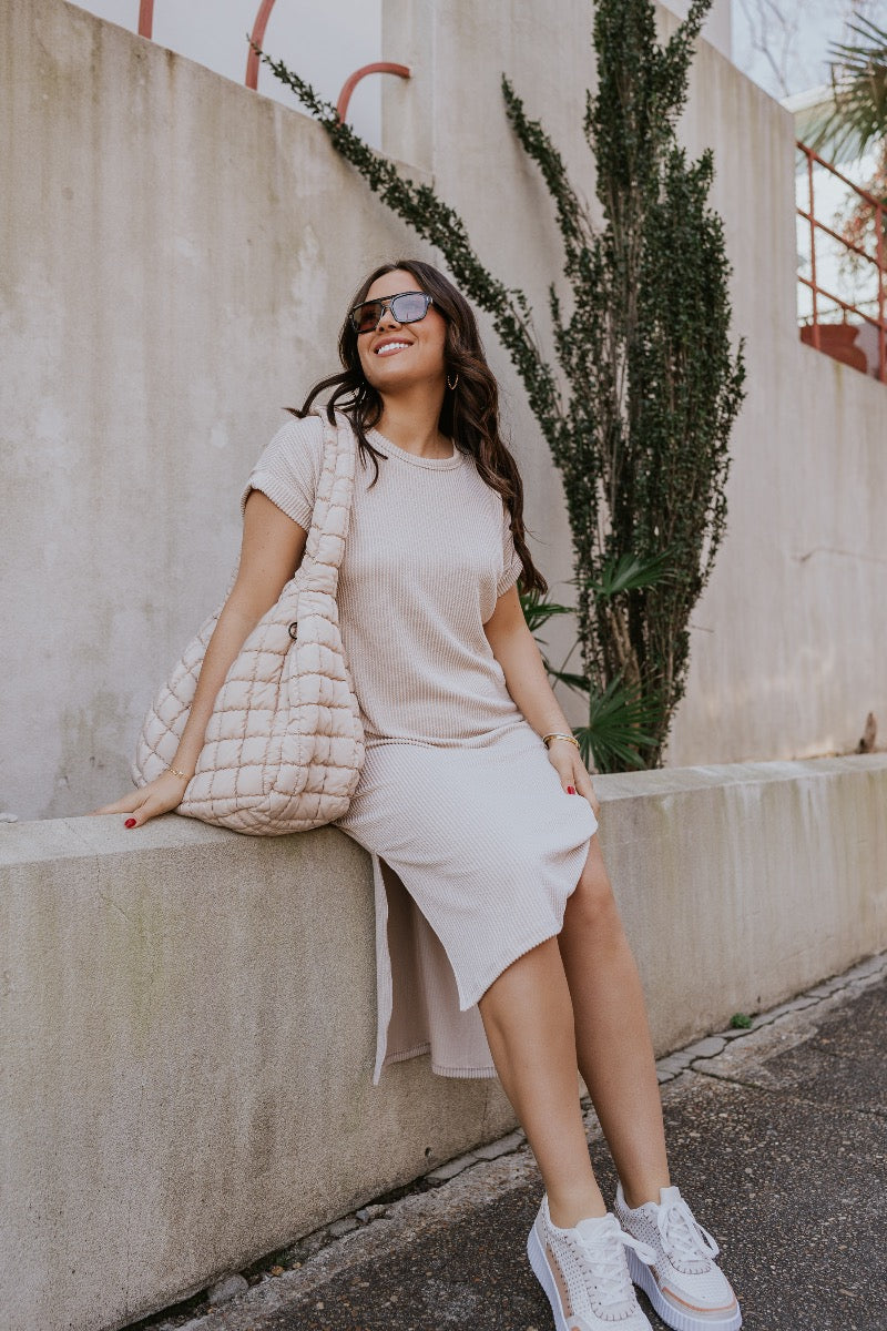 front view of model wearing The Cecile Ribbed Midi Dress features light beige and dark beige textured ribbing, a round neckline, short sleeves with cuffs, side slits, and a slight high-low hemline.