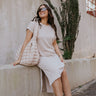front view of model wearing The Cecile Ribbed Midi Dress features light beige and dark beige textured ribbing, a round neckline, short sleeves with cuffs, side slits, and a slight high-low hemline.