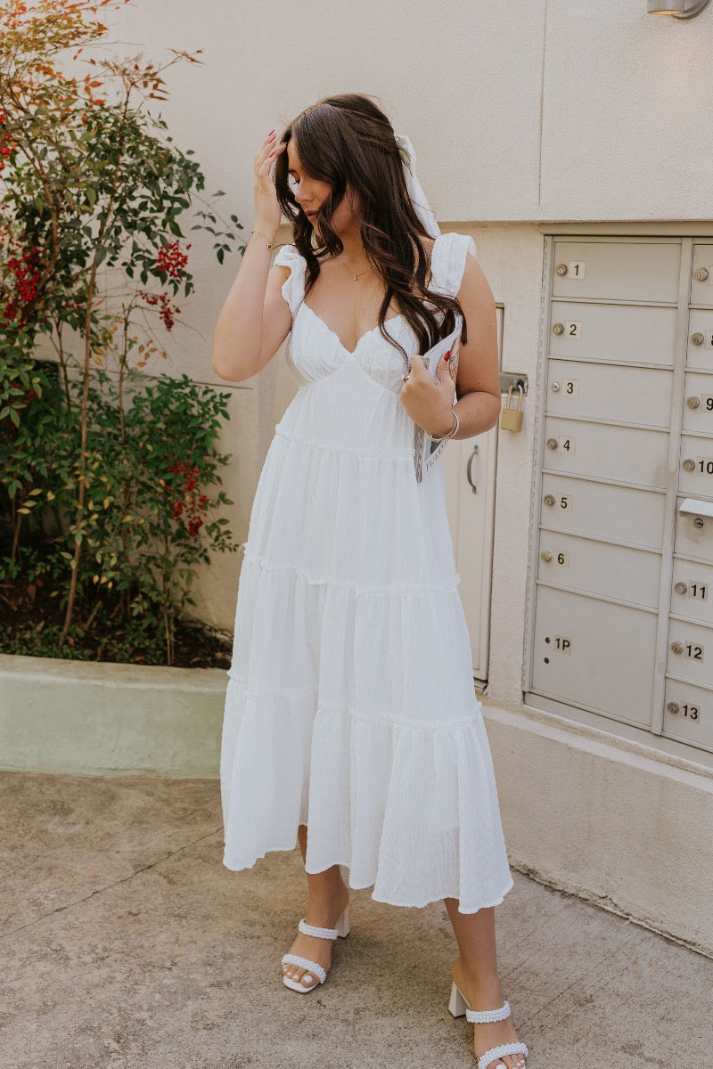 front view of model wearing The Santorini White Maxi Dress features textured off white fabric, maxi length, off white lining, tiered ruffle hem details, sweetheart neckline, ruffle straps and sleeveless.
