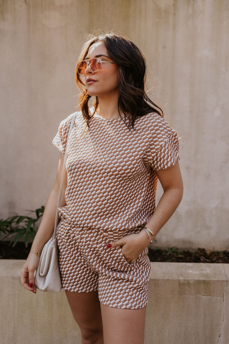 front view of model wearing The Corsica Knit Checkered Top features light brown and off white textured knit fabric, skinny checkered pattern, thick hem, round neckline and short sleeves.